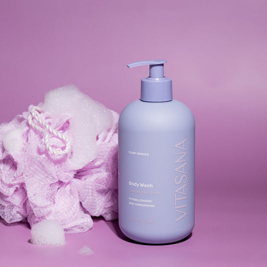 16 fl oz pump bottle of Vitasana Lavender Citrus Body Wash, on a pink-purple background next to a pink loofah. Bottle features the Vitasana logo on a purple background.