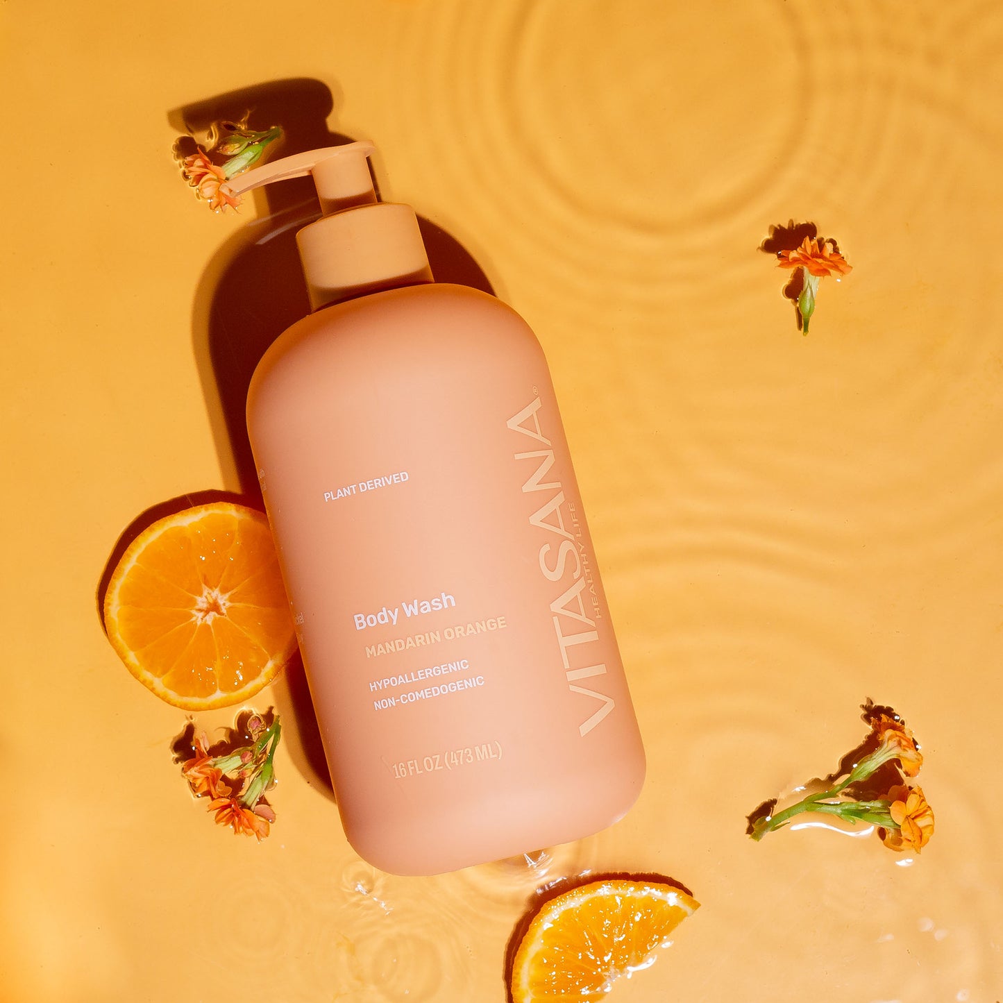 16 fl oz pump bottle of Vitasana Mandarin Orange Body Wash, on an orange background surrounded by orange slices and flowers. Bottle features the Vitasana logo on an orange background.