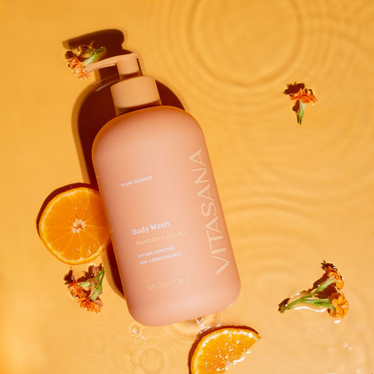 16 fl oz pump bottle of Vitasana Mandarin Orange Body Wash, on an orange background surrounded by orange slices and flowers. Bottle features the Vitasana logo on an orange background.