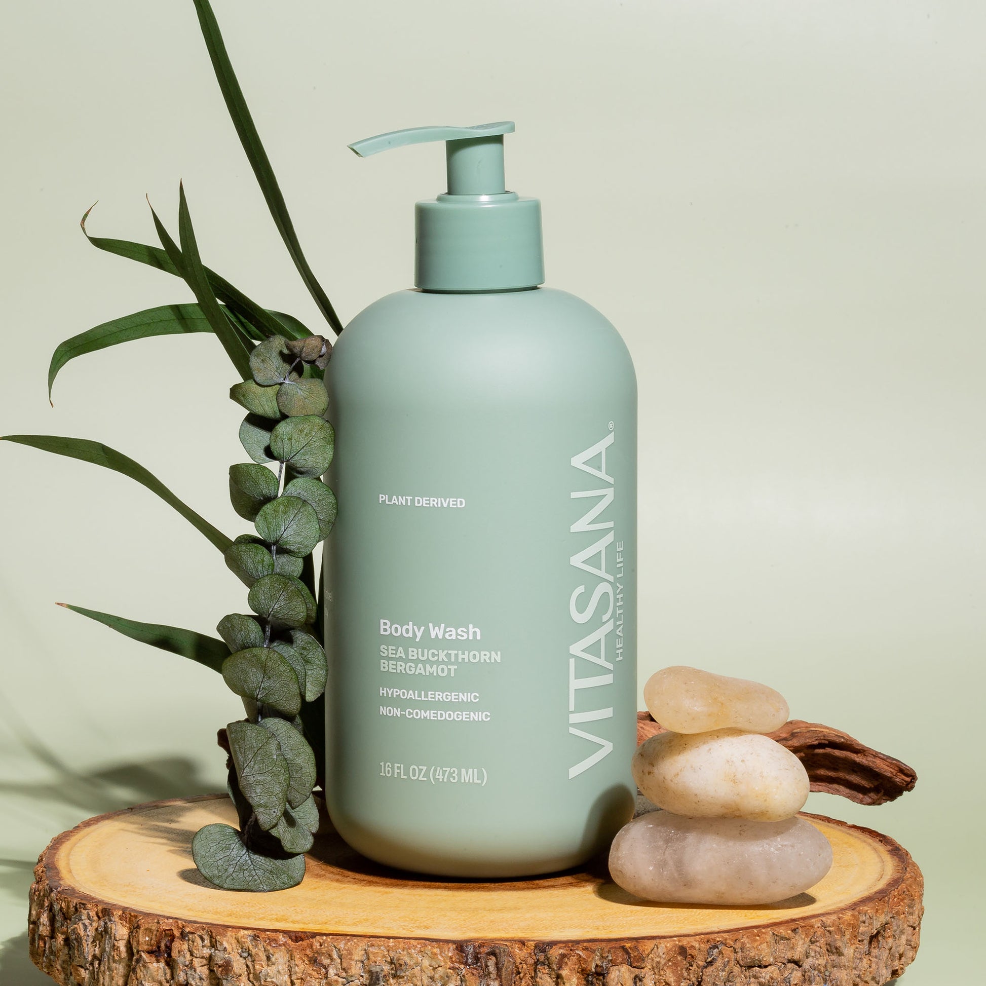 16 fl oz pump bottle of Vitasana Sea Buckthorn Bergamot Body Wash, on a slice of wood with several stones and leaves. Bottle features the Vitasana logo on a pale green background.
