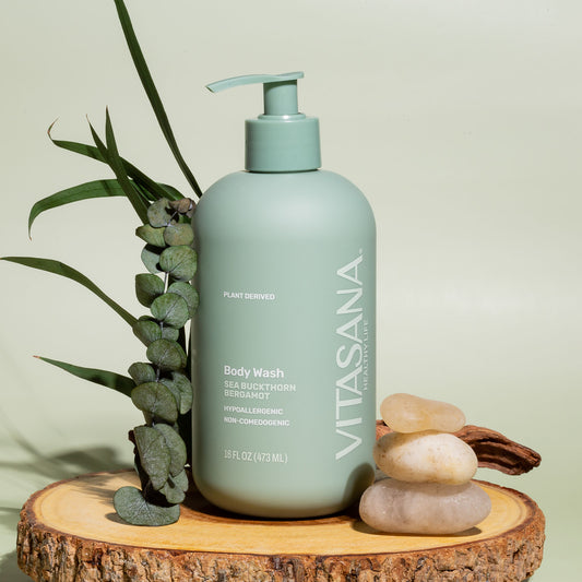 16 fl oz pump bottle of Vitasana Sea Buckthorn Bergamot Body Wash, on a slice of wood with several stones and leaves. Bottle features the Vitasana logo on a pale green background.